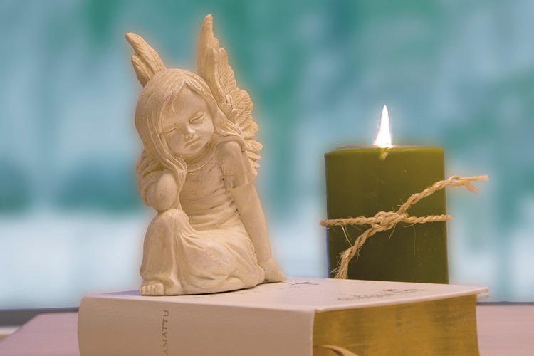 Pieni enkeli patsas raamatun päällä, taustalla palaa kynttilä.