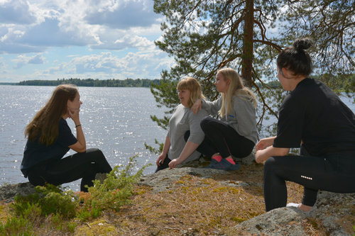 Nuoret istuskelevat kivillä järven rannalla.